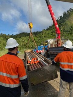 Two workers in safety gear overseeing pipe handling at a construction site.