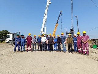 Group of workers and engineers posing at a construction site with cranes in the background.